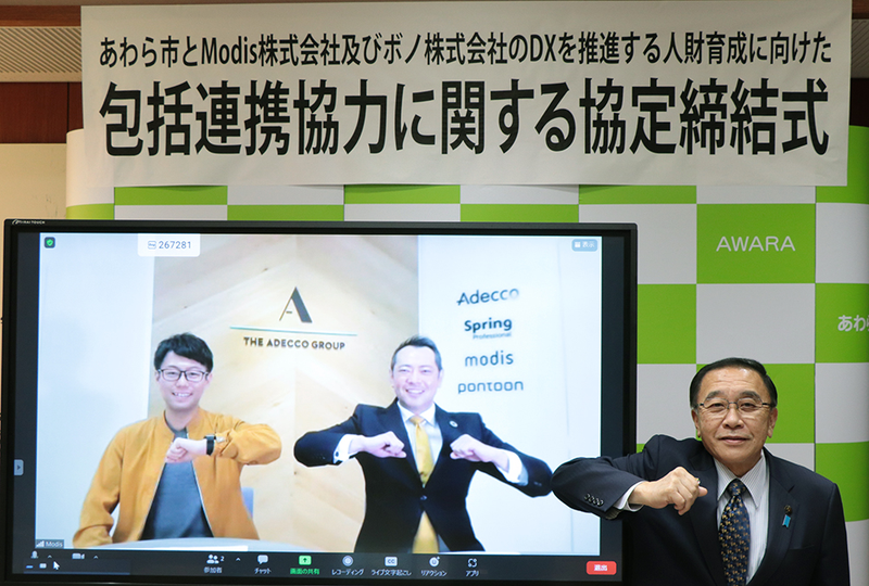 モニターに映る株式会社ボノの谷津氏とModis社長の川崎、モニターの横に座るあわら市の森市長。