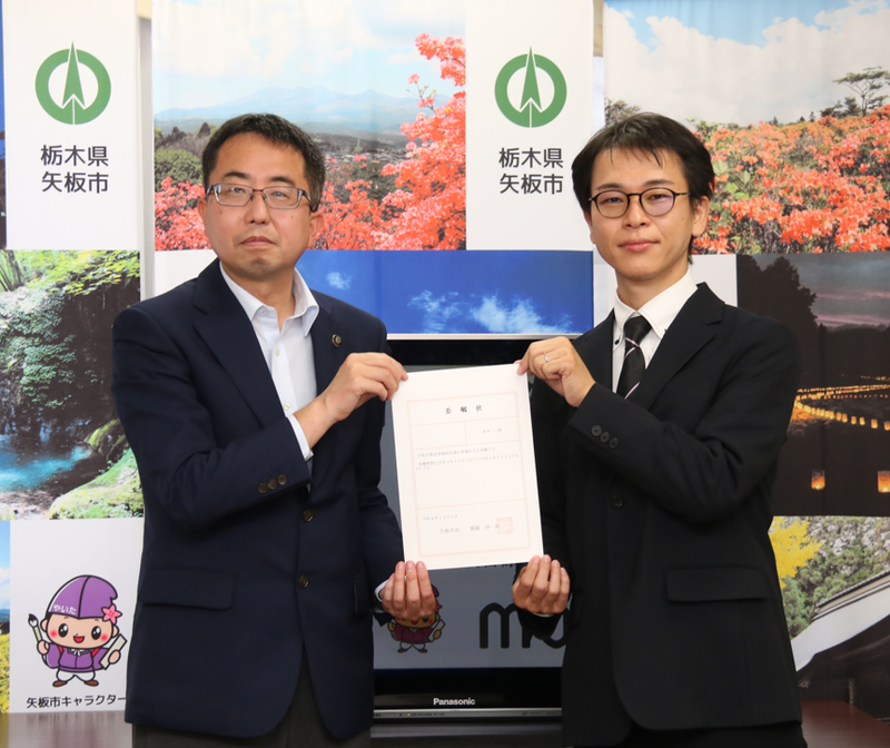 並んで立つ男性二人。二人で一枚の委嘱状を持っている。