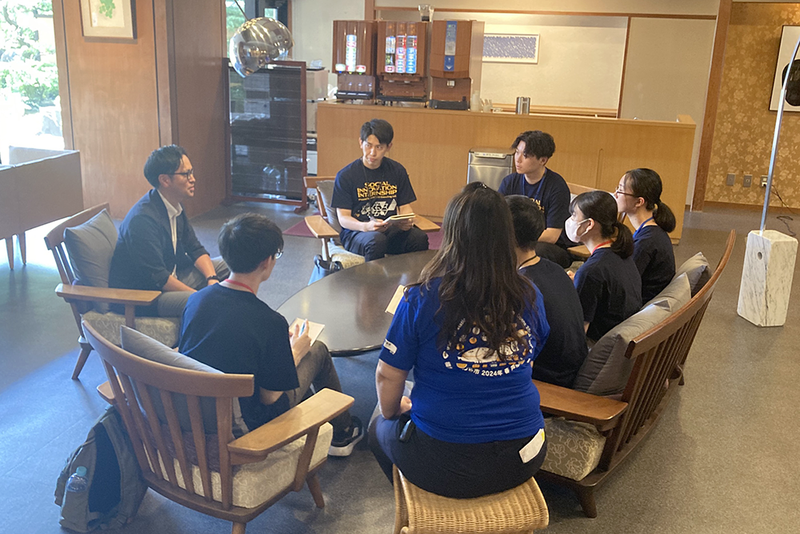 円形のテーブルを囲んで複数人が座り、ノートを取りながらグループワークをしている。