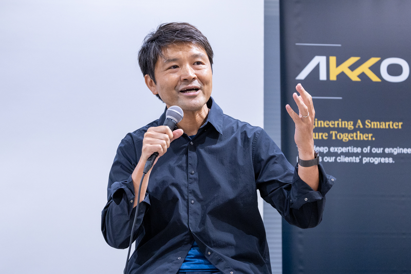 セミナー登壇者がマイクを持ち、片手を上げて説明している様子