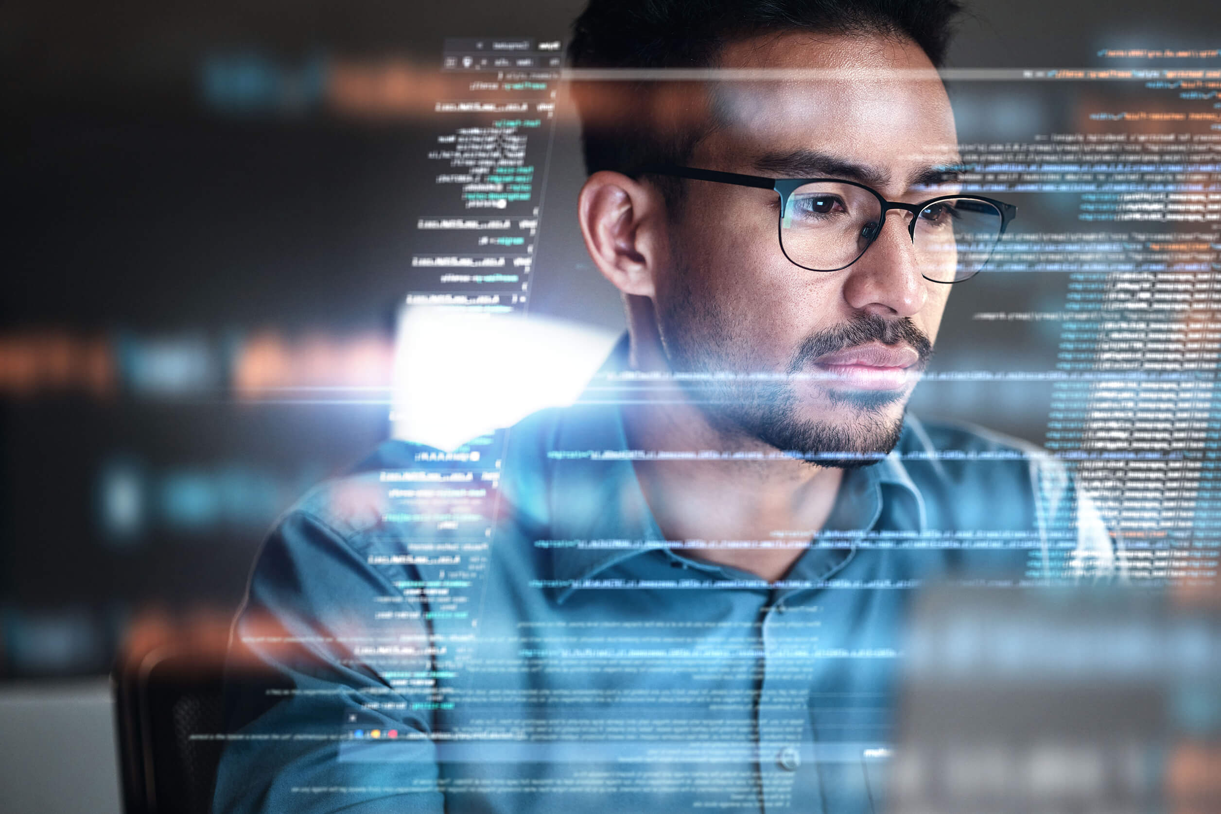 Male sitting in front of a computer screen with software code.