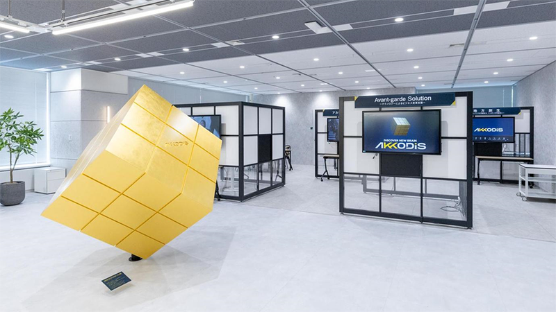 AKKODiS innovation Lab.の写真。左側に、人ほどの大きさの黄色いキューブ型のオブジェが設置されており、各ブースにはモニターと椅子が設置されている。